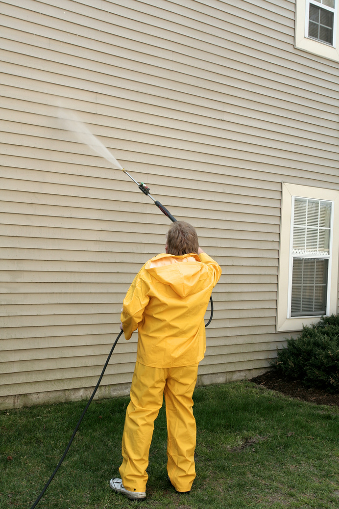 A worker pressure washing the siding of a house